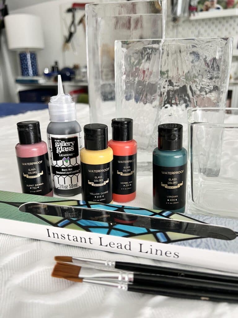 Supplies to paint a glass vase that include glass paint, liquid lead, stained glass lead lines.