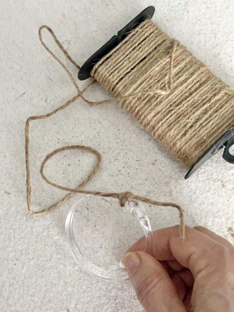 Knotting the end of jute twine to a plastic curtain ring.