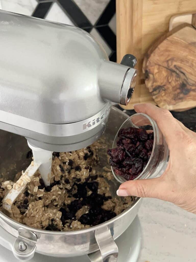 Pouring dried cranberries into a bakery style chewy oatmeal raisin cookie recipe dough.