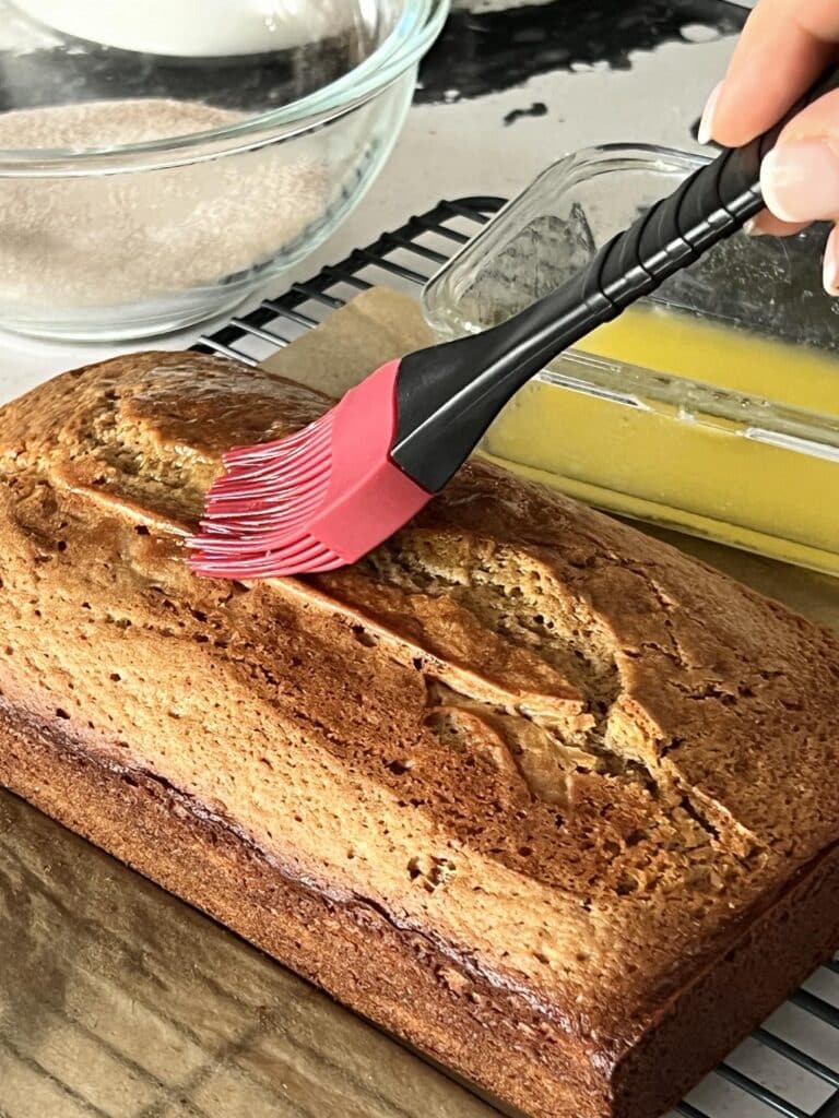 Brushing an apple cider donut bread loaaf with melted butter.