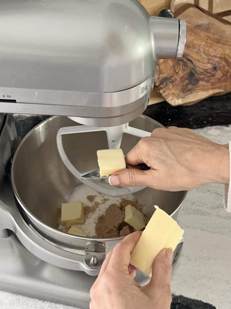 Slicing butter into mixer for chewy oatmeal raisin cookies recipe for a bakery style flavor.