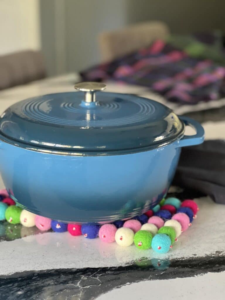 Blue cast iron dutch oven sitting on top of a handmade wool ball trivet.