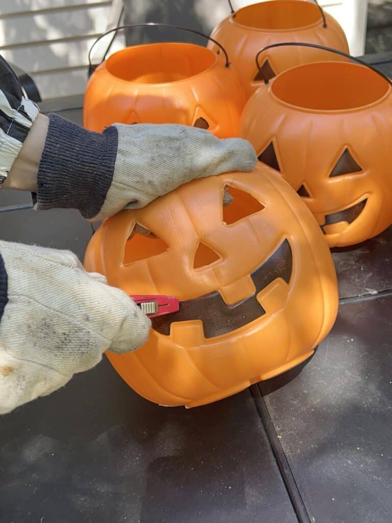 Cutting out of eyes, nose, and mouth of pumpkin pails for these DIY pumpkin porch decorations.