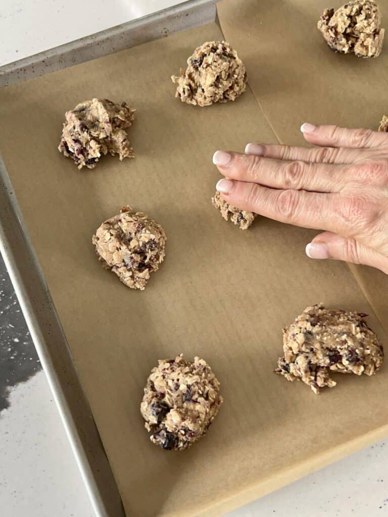 Flattening oatmeal raisin cookie dough on a parchment covered baking sheet.