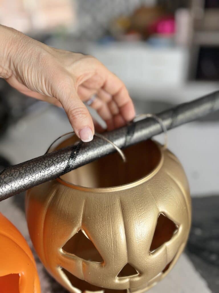 Twisting pumpkin pail handle onto tension rod for DIY pumpkin porch decorations.