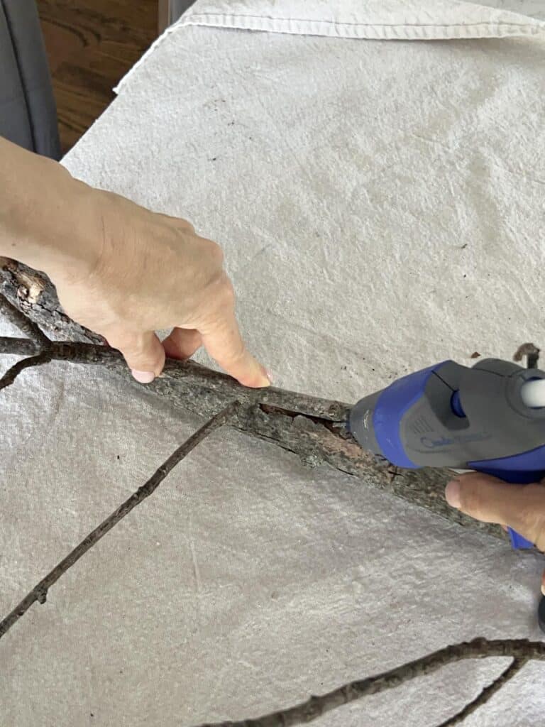 Applying hot glue to connect tree branches for a decor idea.