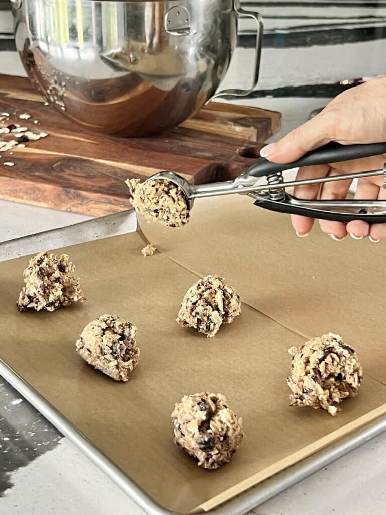 Scooping chewy oatmeal raisin cookie dough with an ice cream scoop.