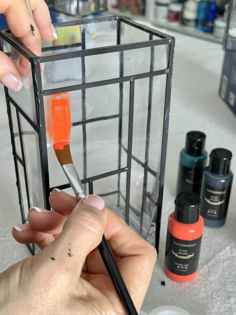 Applying red paint on a glass vase.