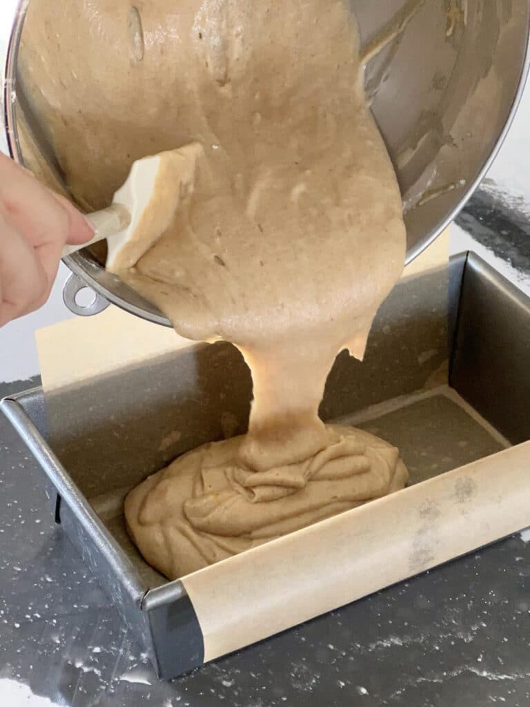 Pouring apple cider donut bread batter into loaf pan for baking.