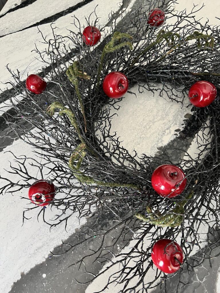 A black twig wreath with red apples.