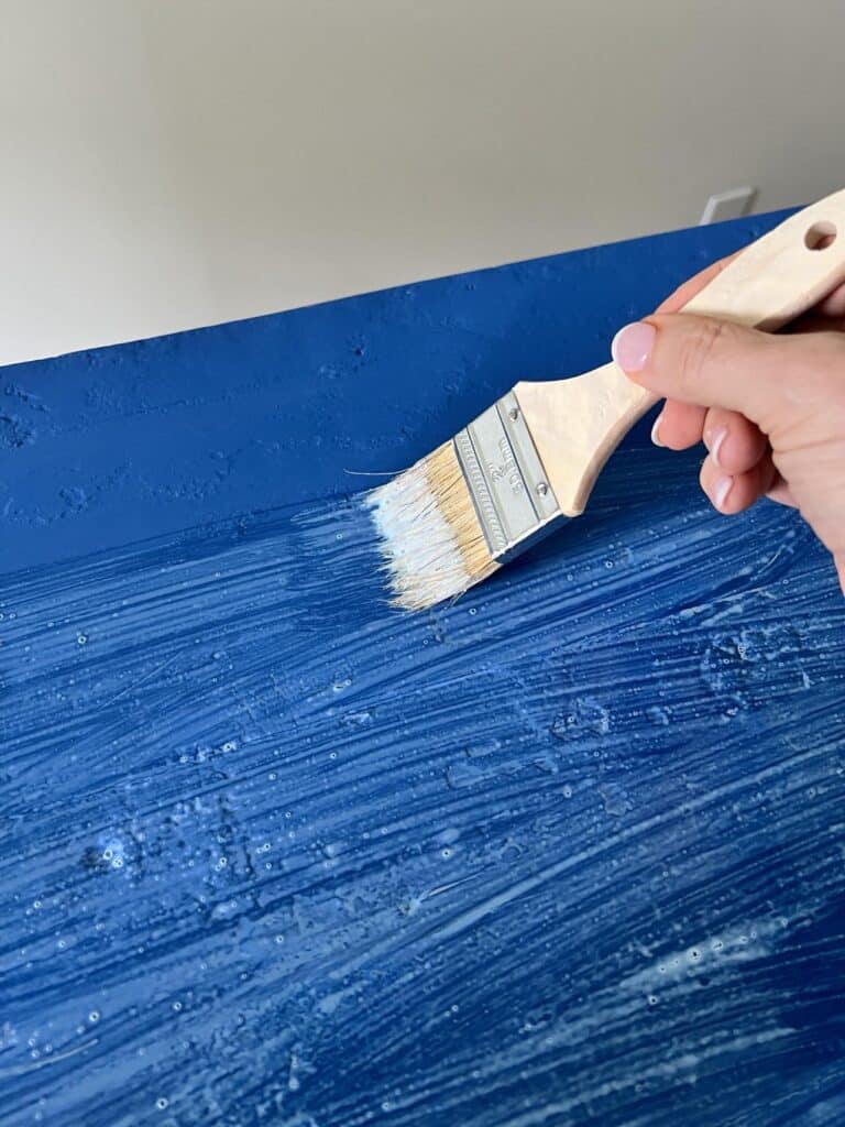 Brushing a topcoat on top of the painted furniture surface.