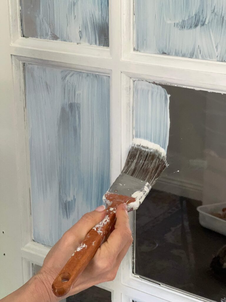 Brushing liquid mask on window panes before painting French doors.