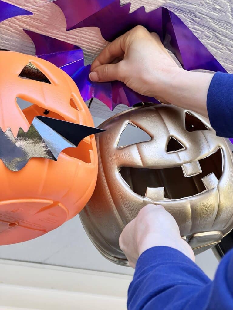 Attaching holographic bats to pumpkin porch decorations.