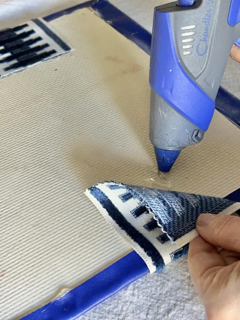 A hot glue applying glue to the back of a diy desk pad to adhere fabric trim.