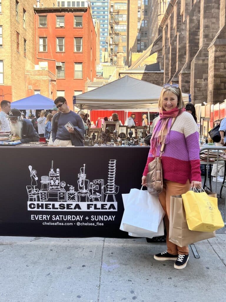 Woman standing beside chelsea flea market manhattan banner.