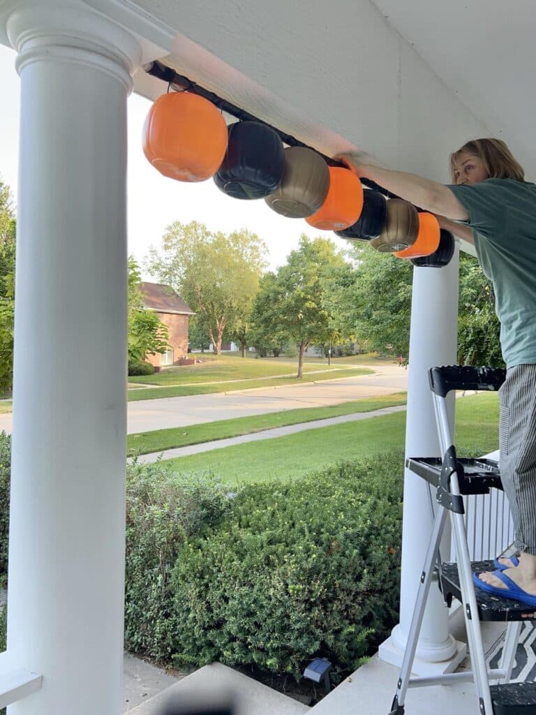 Hanging pumpkin porch decorations tension rod between two pillars on front porch.