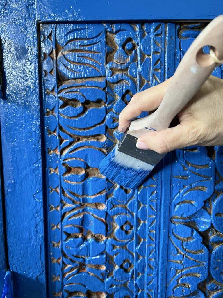 Carved wood doors on the front of a painted furniture piece.