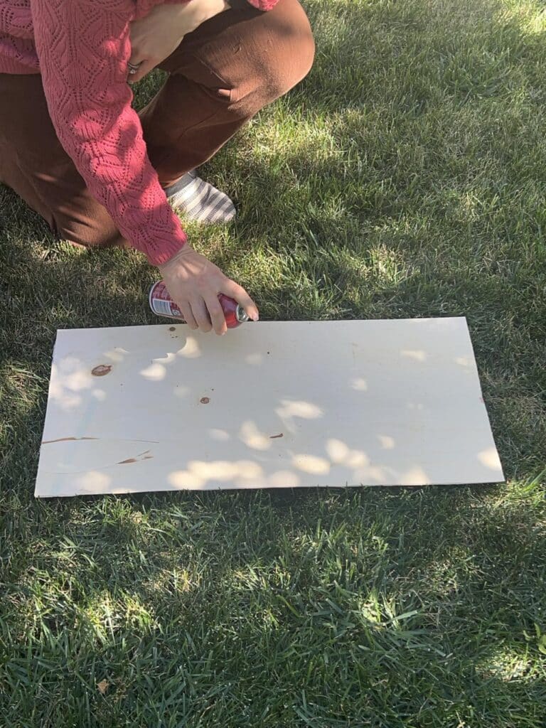 Spraying adhesive to the back of a piece of MDF board.