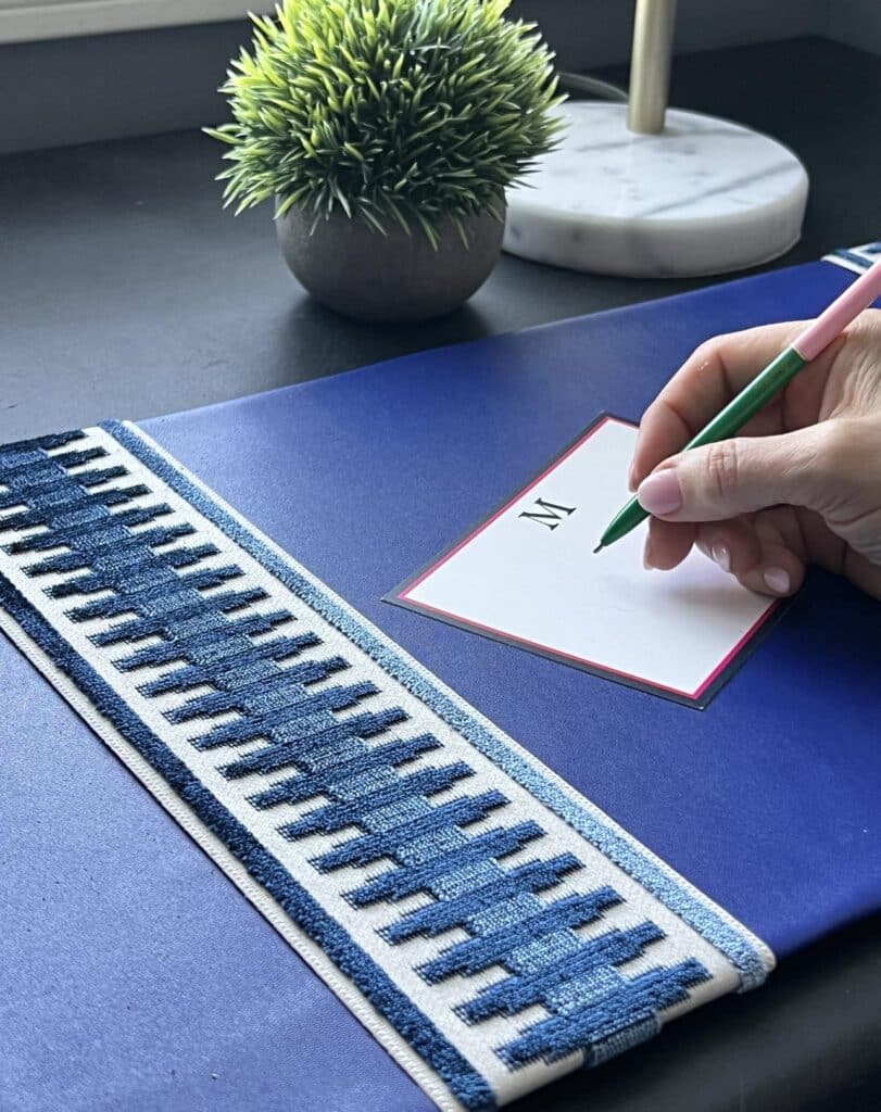 A hand holding a pen and writing a letter on a postcard on top of a diy desk pad.