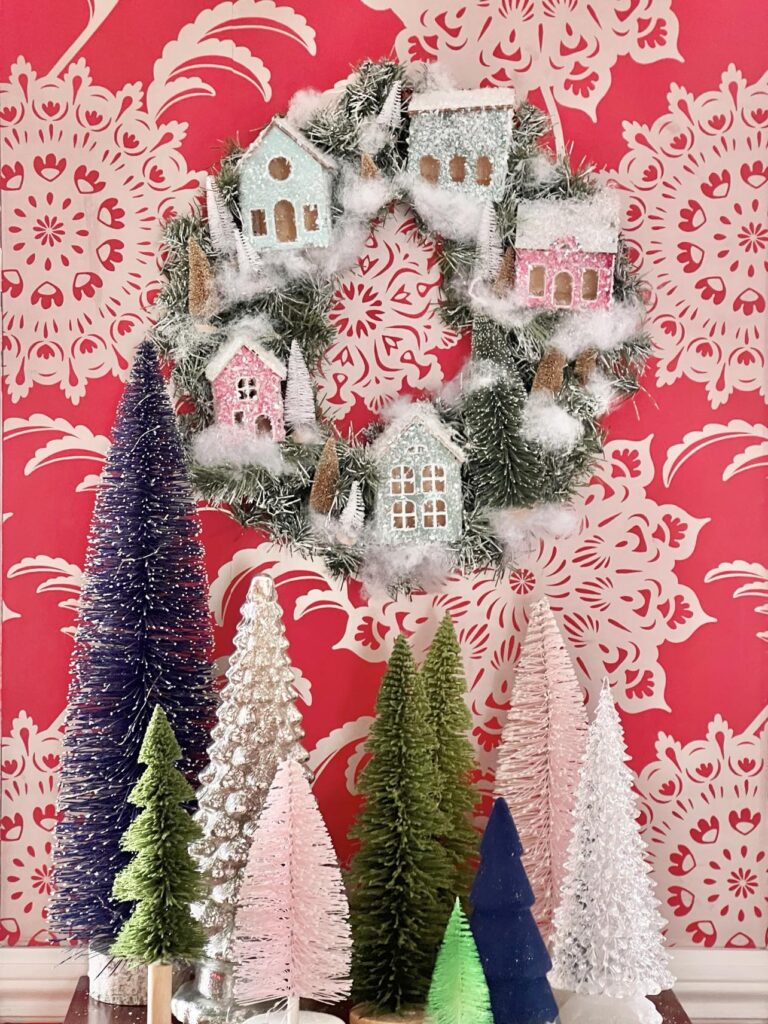 An Anthropologie DIY Christmas Wreath hanging on a bright red wallpaper wall with bottle brush trees.