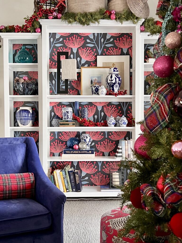 A wallpaper-covered bookcase decorated with chinoiserie pieces fo a Christmas home tour.