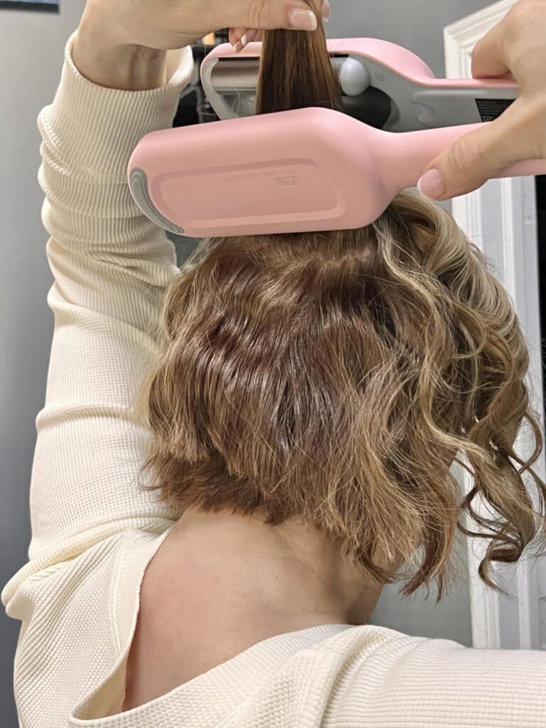 Woman using hair waver tool on the back of her hair to create curls.