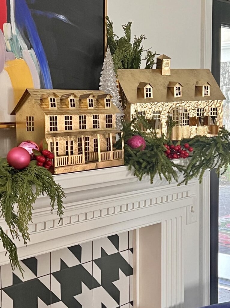 Gold metal decorative houses sitting on a Christmas mantel as part of a home tour.