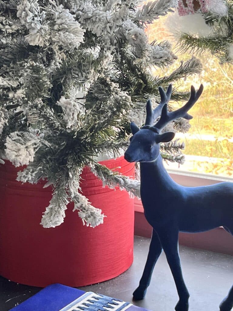 A blue decorative deer standing beside a red lampshade used as Christmas tree collar ideas.