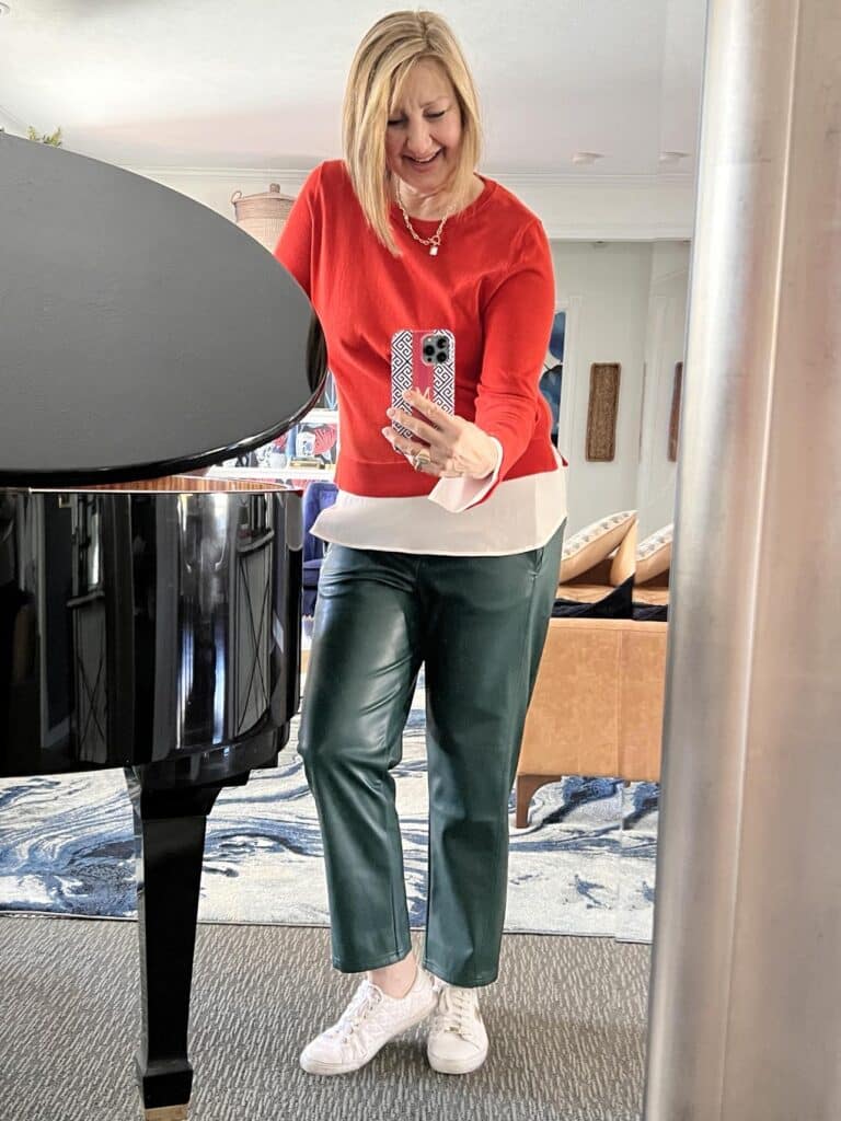 How to wear sneakers: Woman wearing orange sweater, green leather pants, and white faux leather sneakers.