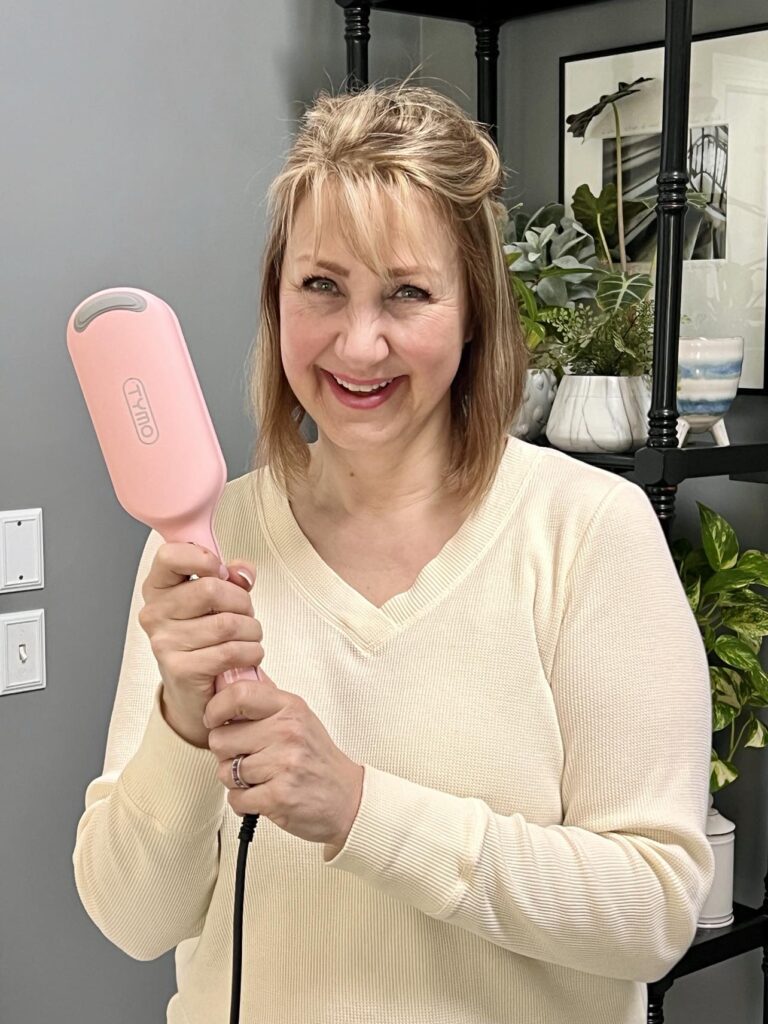 Woman with hair tied back and holding a hair waver tool.