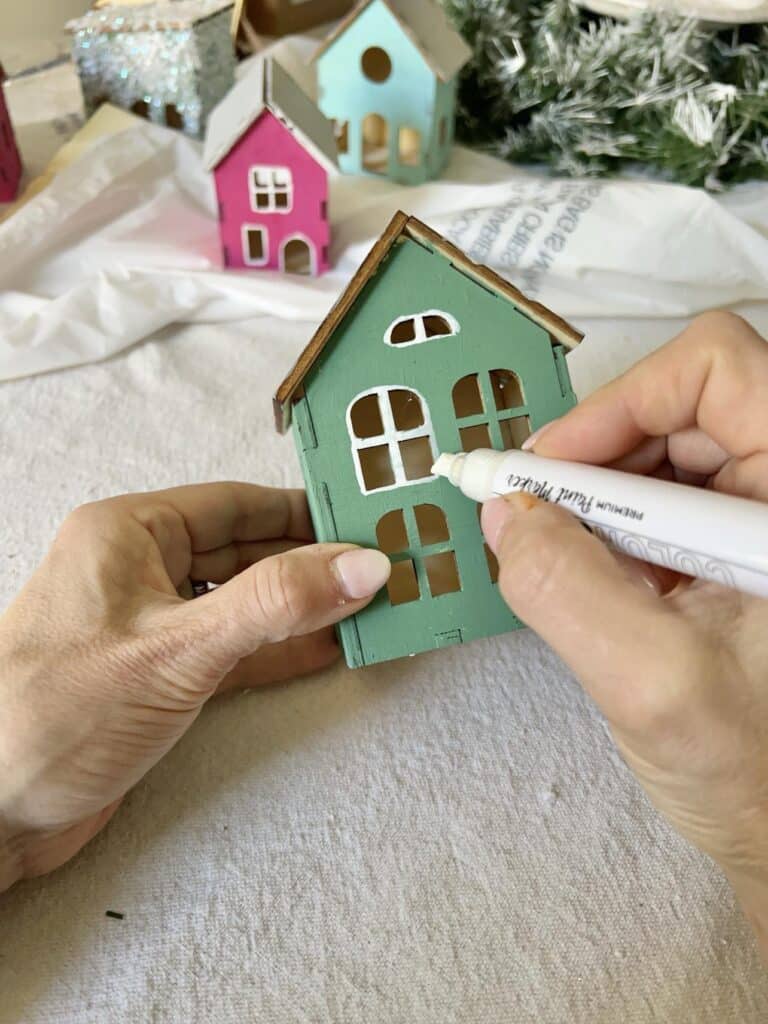 Outlining the window of a painted wood puzzle house with a paint pen.