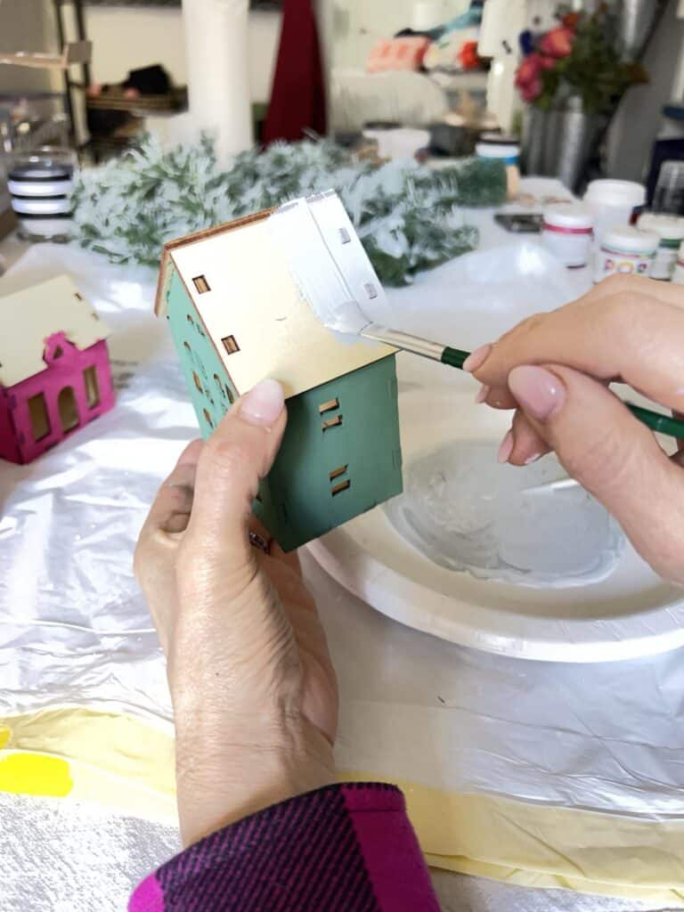 Painting the rooftop of a toy wood house light grey.