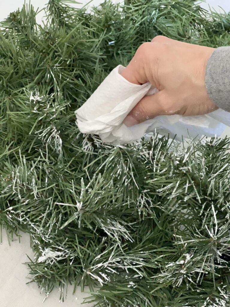 Painting the tips of a green wreath with white paint.