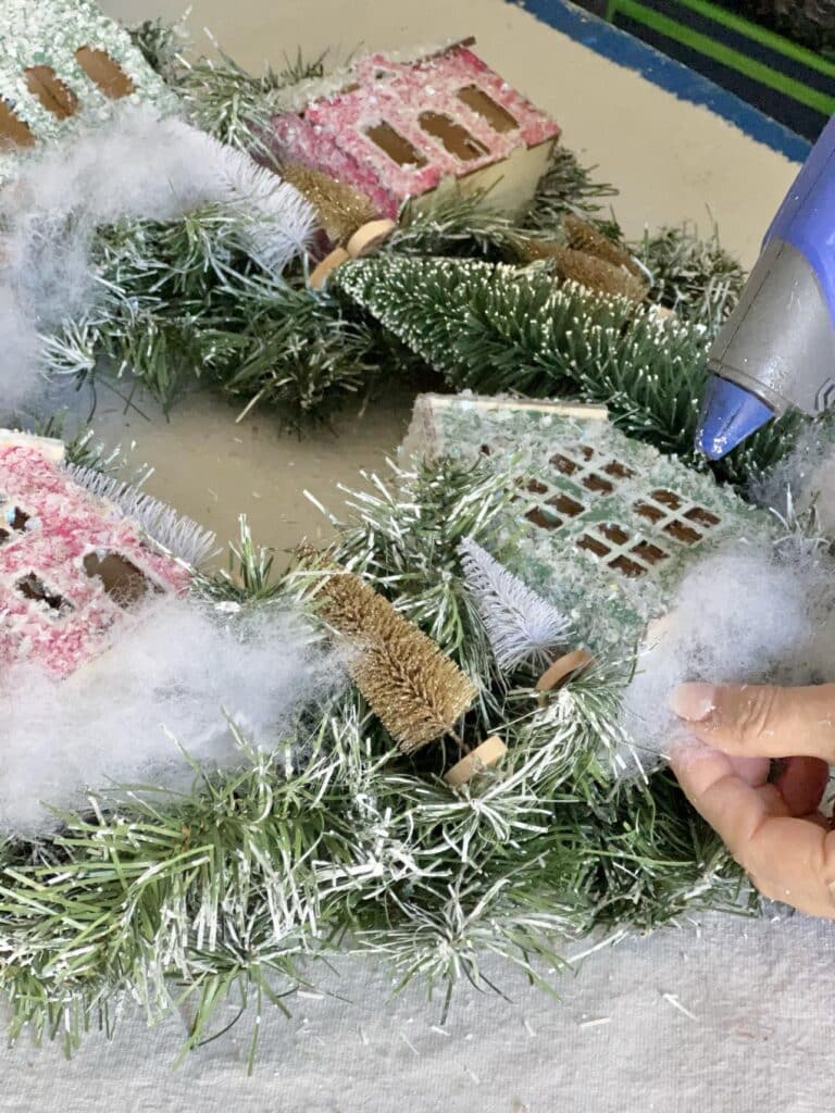 Adding white batting underneath the toy houses in the Anthropologie DIY Christmas Wreath.