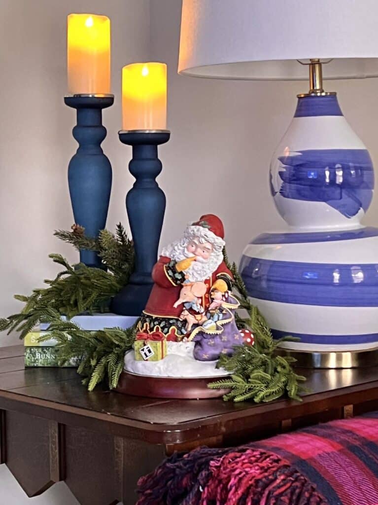 Santa figurine placed on an end table in front of two blue candlesticks.