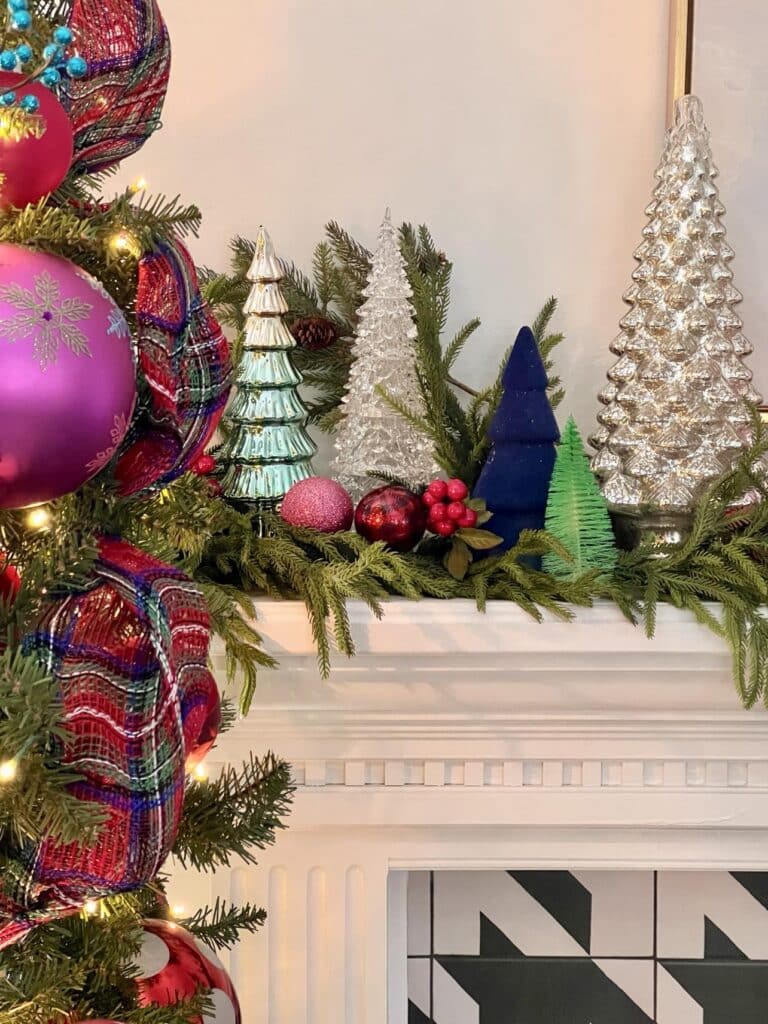 Glass and bottle-brush trees sitting on a fireplace mantel.