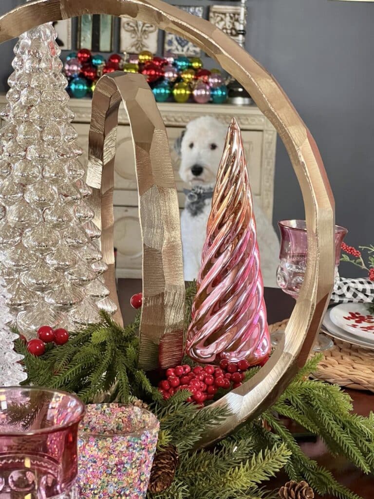 a white dog gazing through the middle of a Christmas table centerpiece.