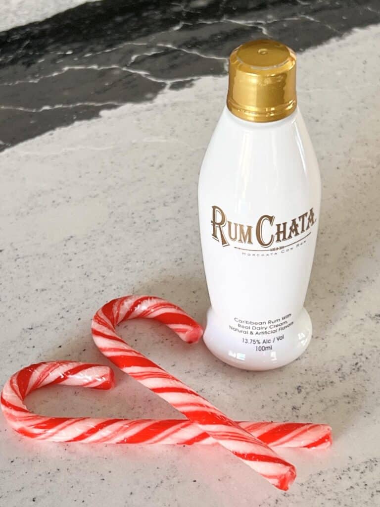 Bottle of RumChata liqueur beside two candy canes.