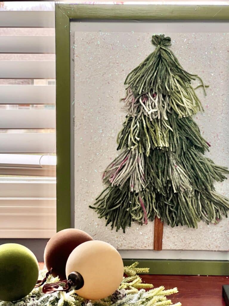 Christmas tree tassel wall art on a table with round ornament balls.