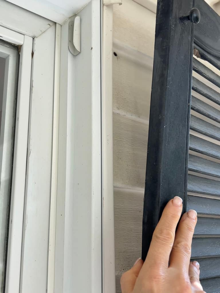 A faded louvered shutter pulling away from the house siding.