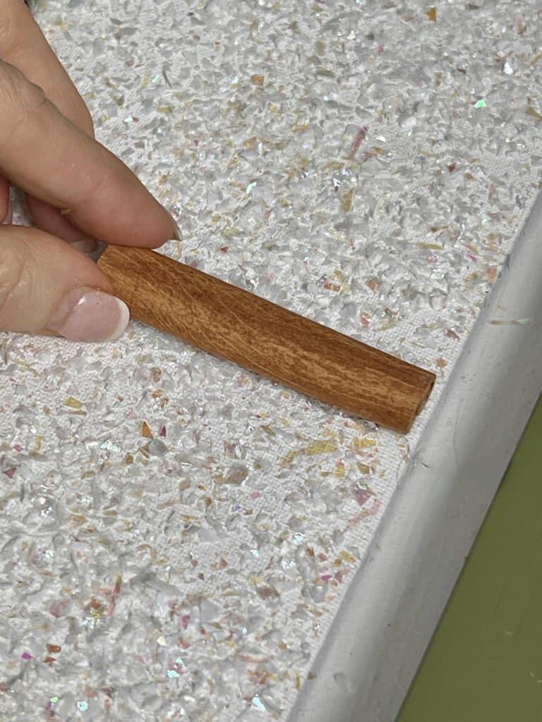 Gluing a cinnamon stick to the bottom of a canvas.