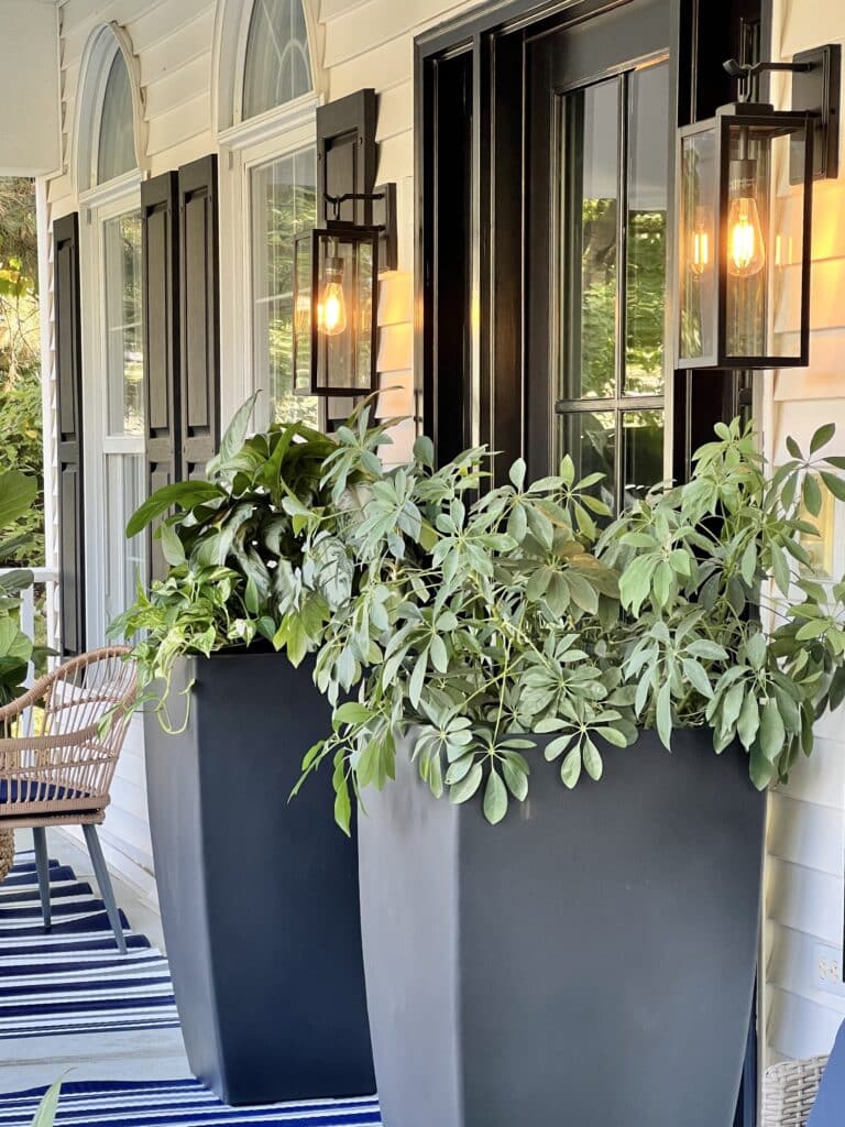 front porch ideas include two outdoor wall sconces and large outdoor pots holding green plants.