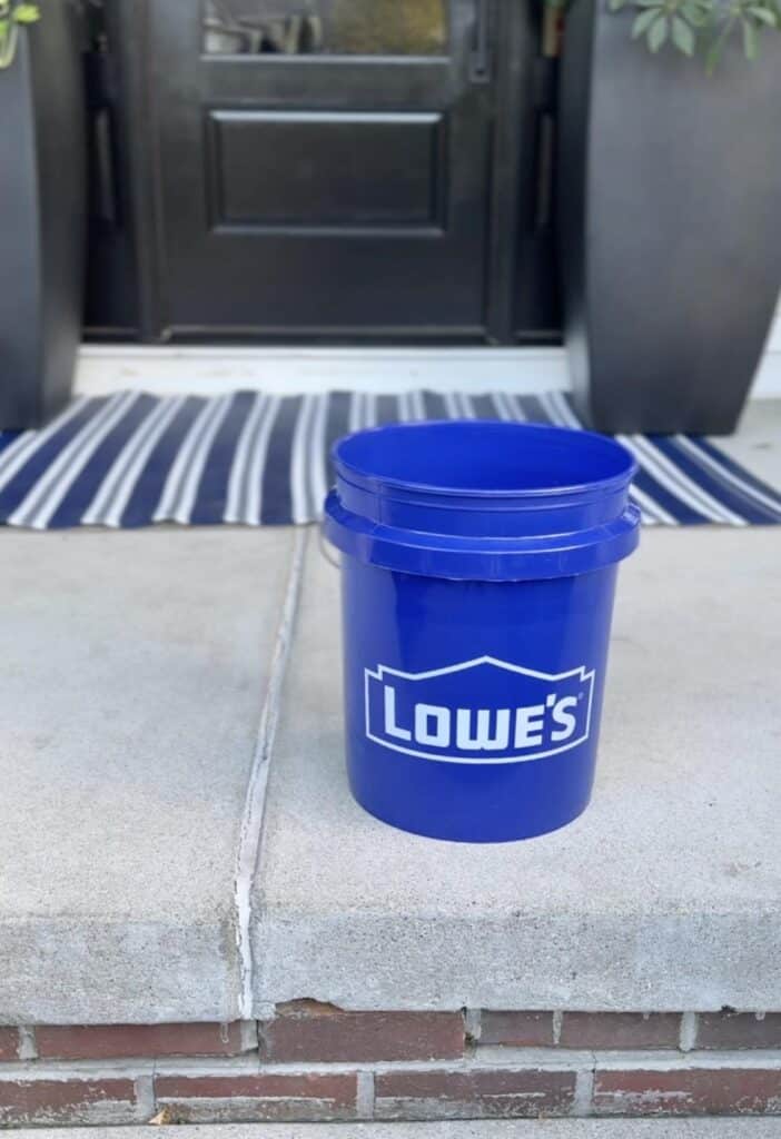 A blue Lowes bucket sitting on a front porch.