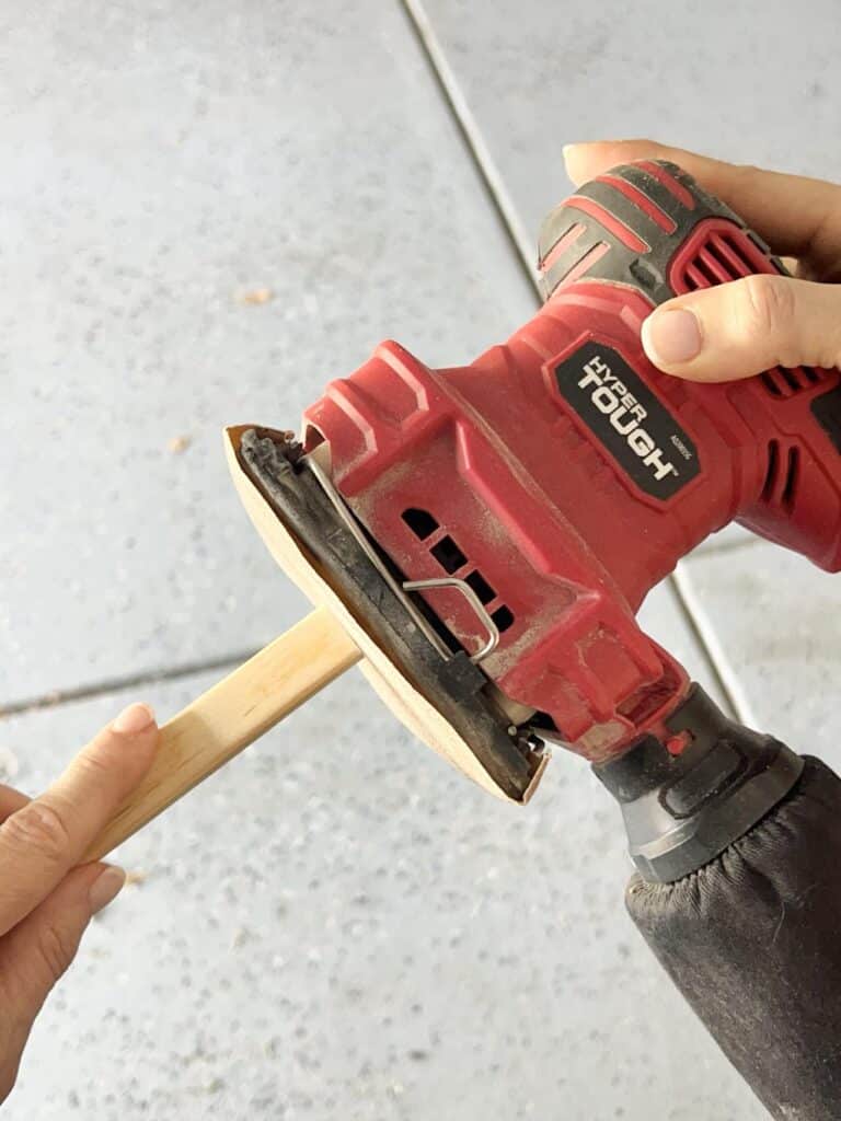 Sanding the edges of cut wood molding piece with a palm sander.