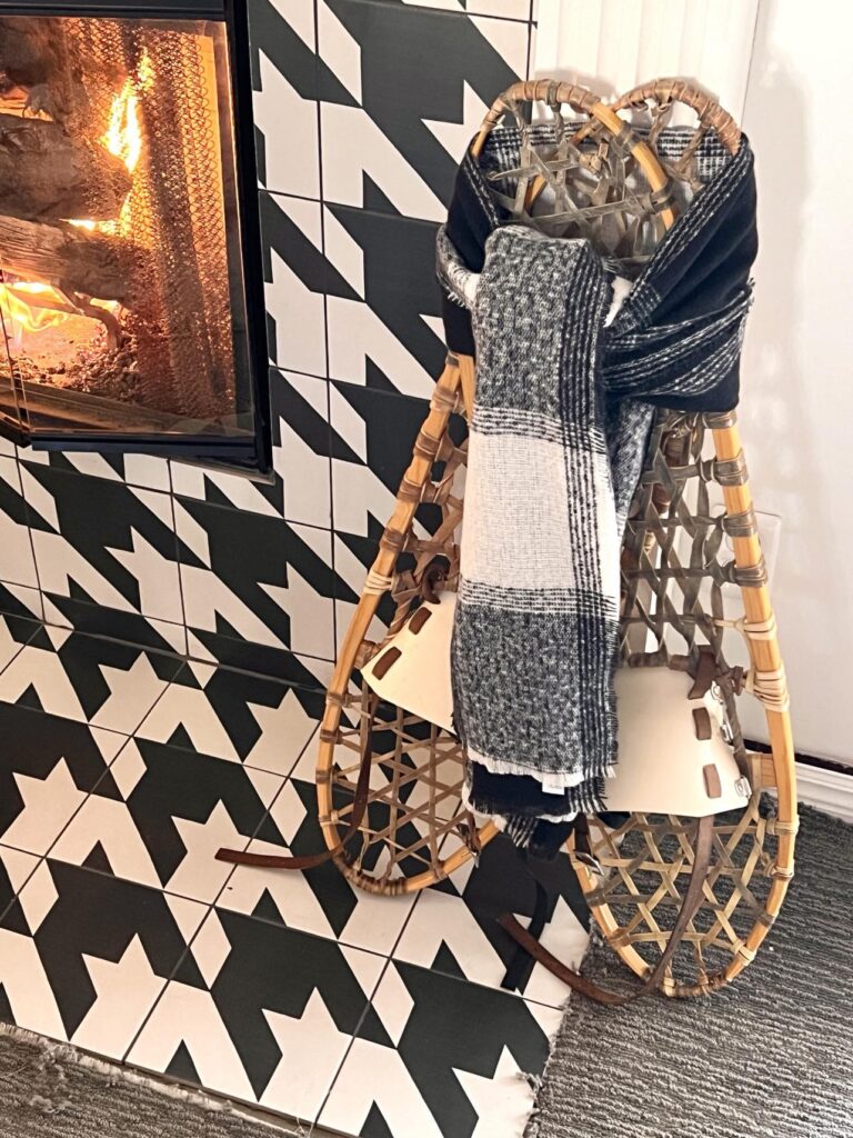 Snowshoes with a black plaid scarf tied around the center for home decorating by a fireplace.