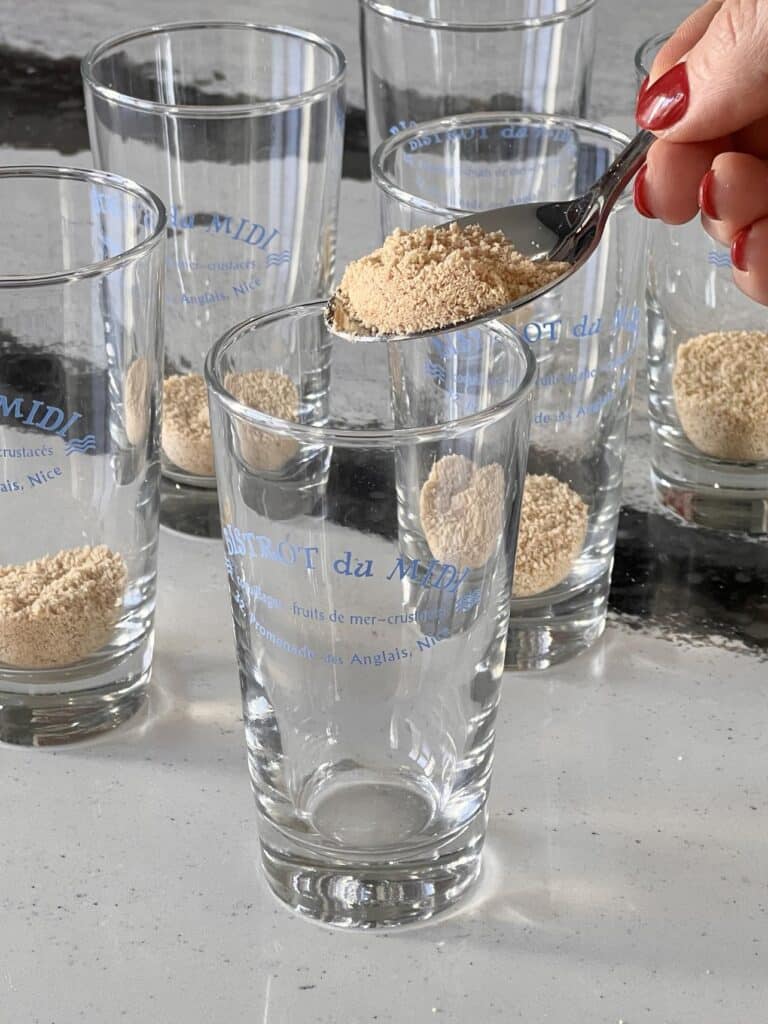 Spooning graham cracker crumbs into shot glasses.