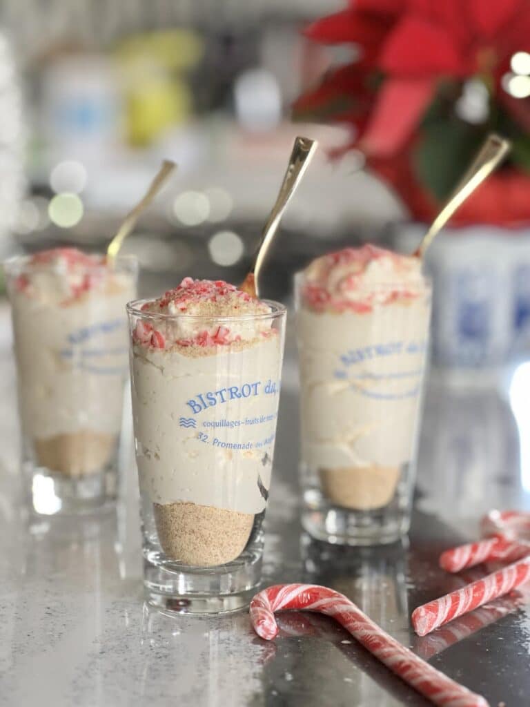 Three RumChata cheesecake pudding shots on a table with candy canes beside them.