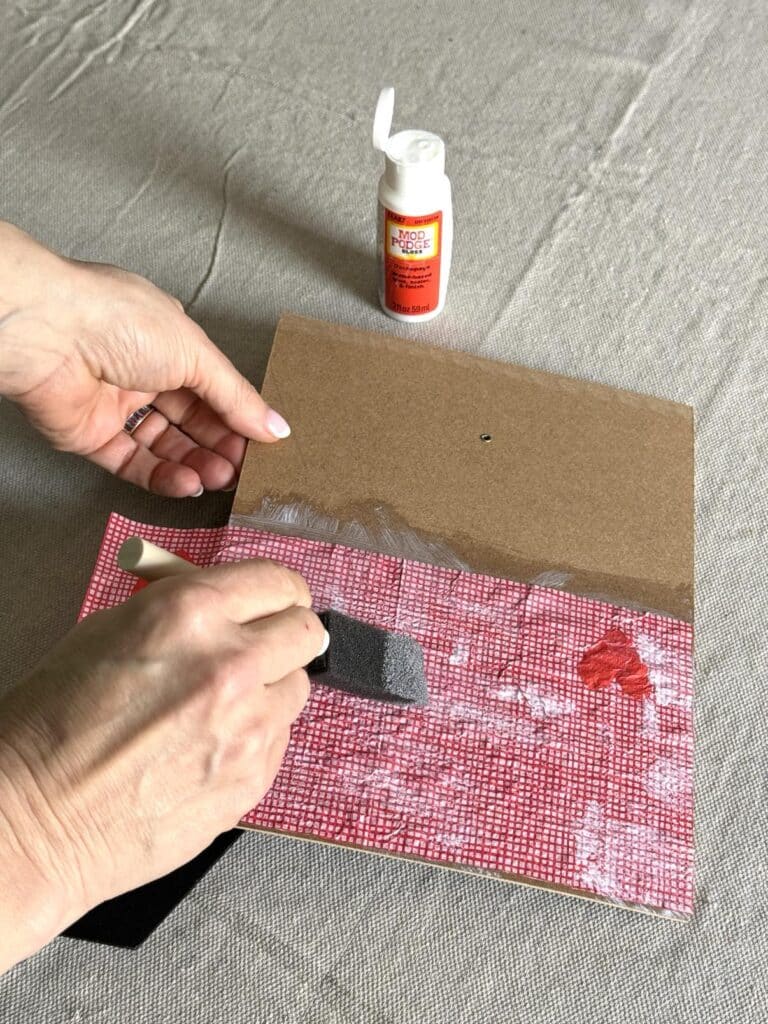 Brushing decoupage glue across a paper napkin on the back of a photo frame.