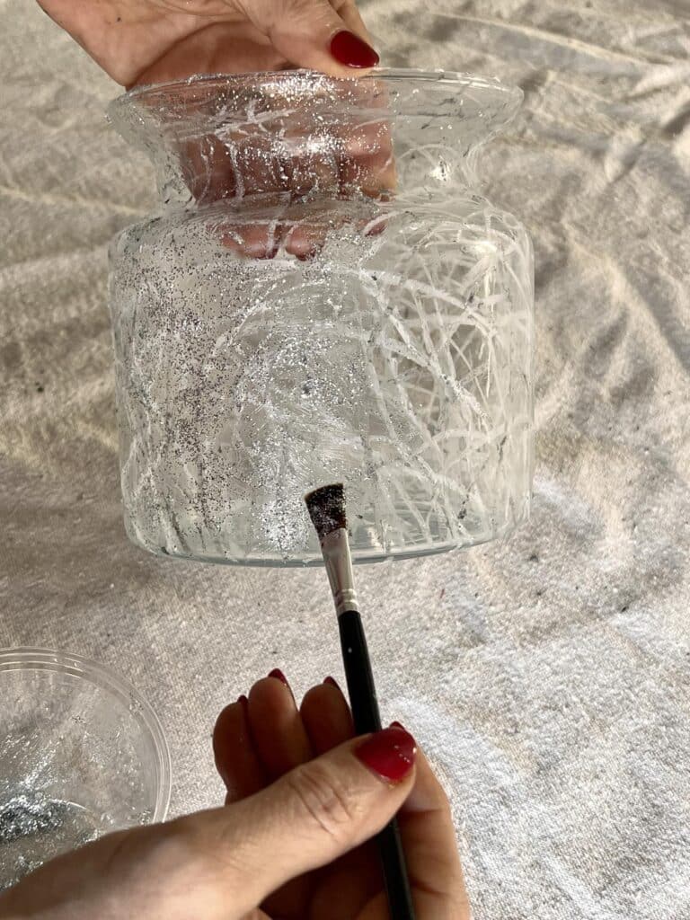 Brushing glitter glue onto the outside of a vase.