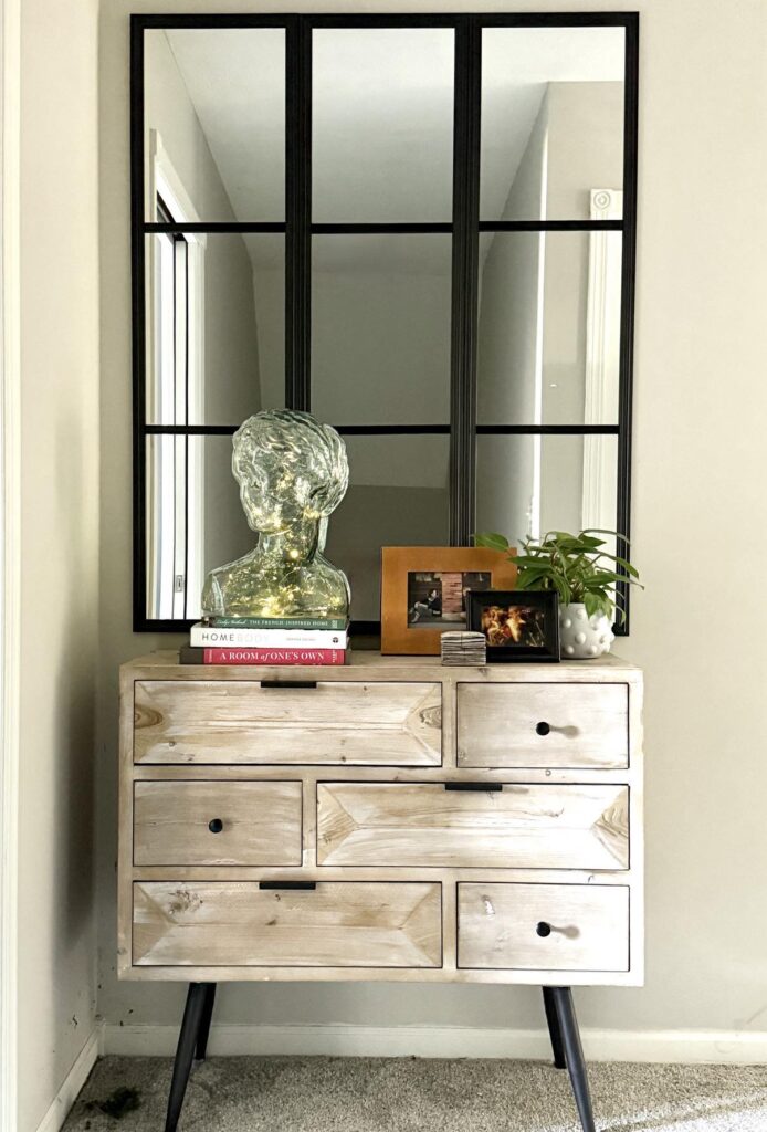 A completed grid mirror hack hanging above a side table with photographs and plant.